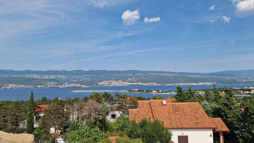 View over rooftops and trees to a bay and mountains