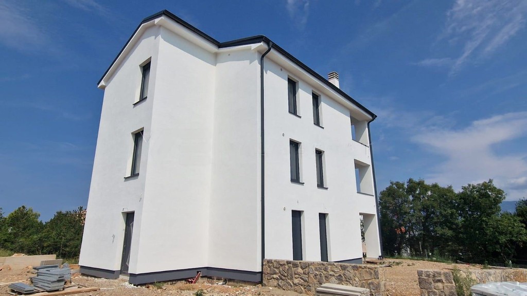 White rendered three-storey building with dark windows and a stone wall