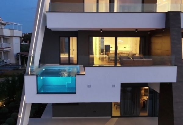 Modern seafront property in Croatia at dusk with illuminated infinity pool and multi-story facade.