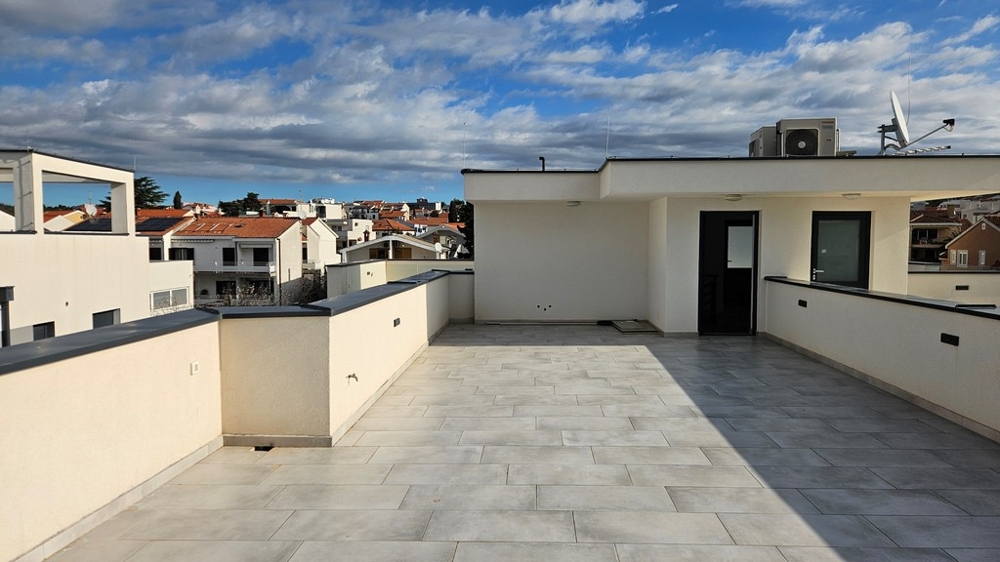 Large, private roof terrace of a penthouse for sale in Zadar, Croatia, surrounded by buildings under an overcast sky