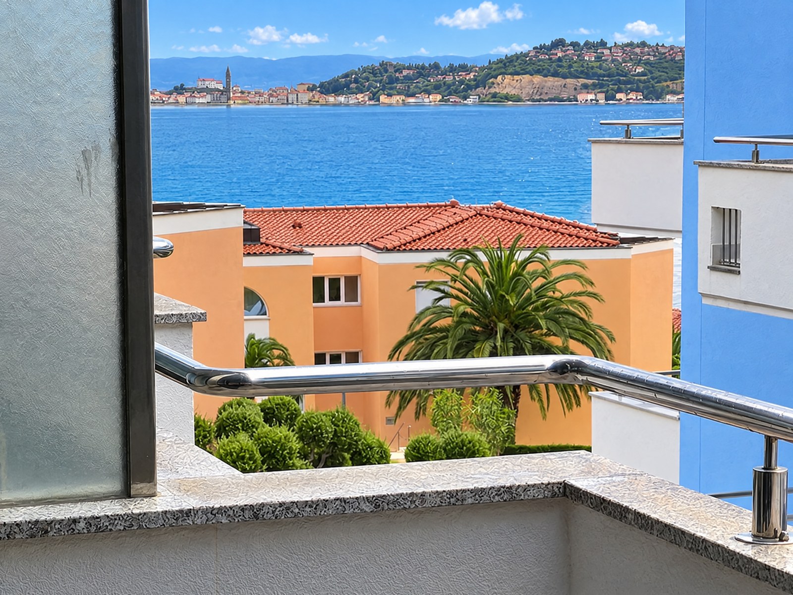View from the balcony over a palm tree and rooftops to the sea