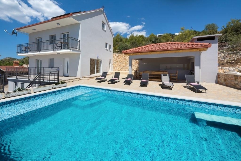 View of the infinity pool, sunbathing area with covered dining area, and the house.