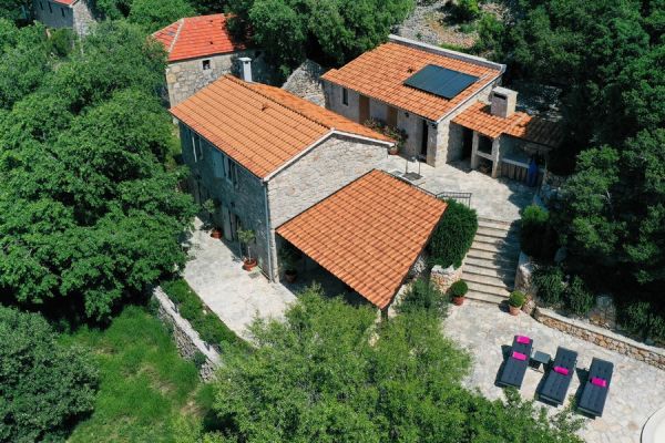 Aerial view of a traditional Croatian stone house for sale with outbuildings and terracotta roofs surrounded by green areas.