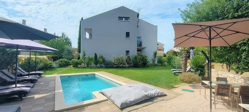 Pool area of ​​the three-apartment house in Istria for sale, with sun loungers, parasol and a well-maintained lawn.