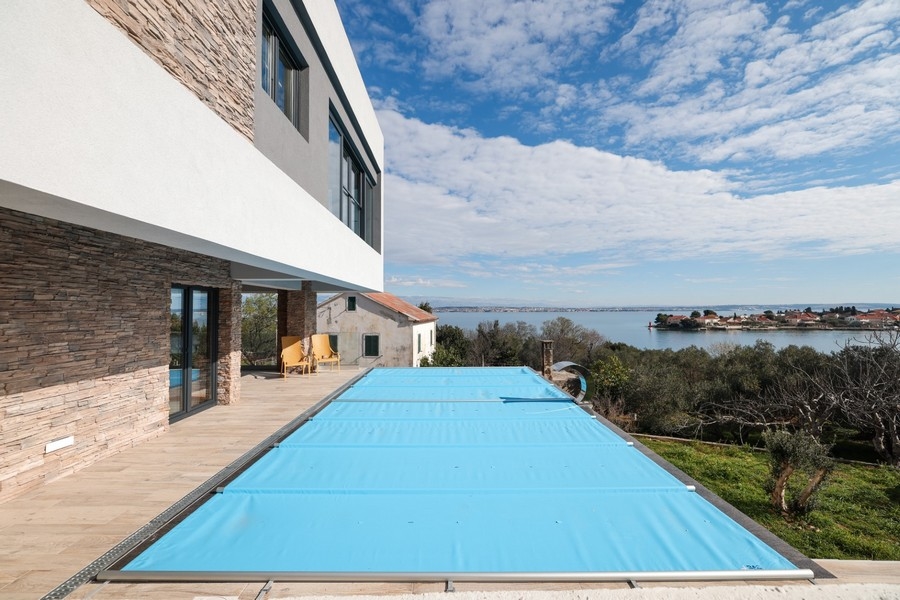 Exterior view of a modern villa with pool for sale on Ugljan island in Croatia, sea view and blue sky in the background.