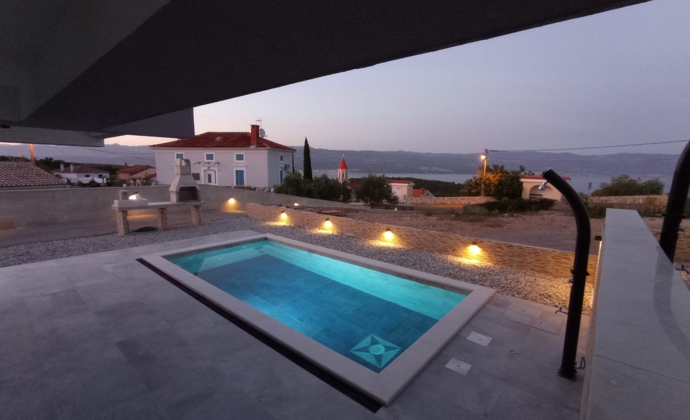 Evening view of a property in Croatia with illuminated pool and the sea in the background.