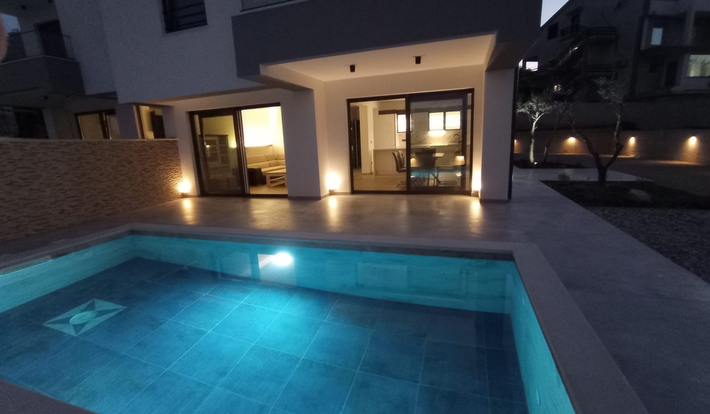 Dusk view of the terrace and pool of a property in Croatia, interior lighting creates an inviting atmosphere.
