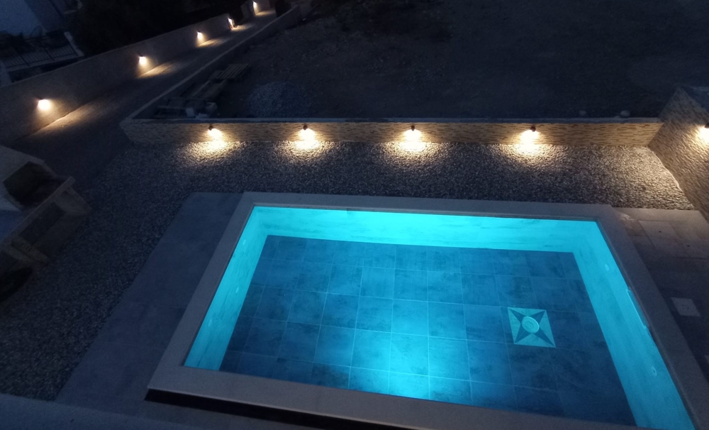 Night view of a pool with blue lighting and a partial view of the property in Croatia in the background.