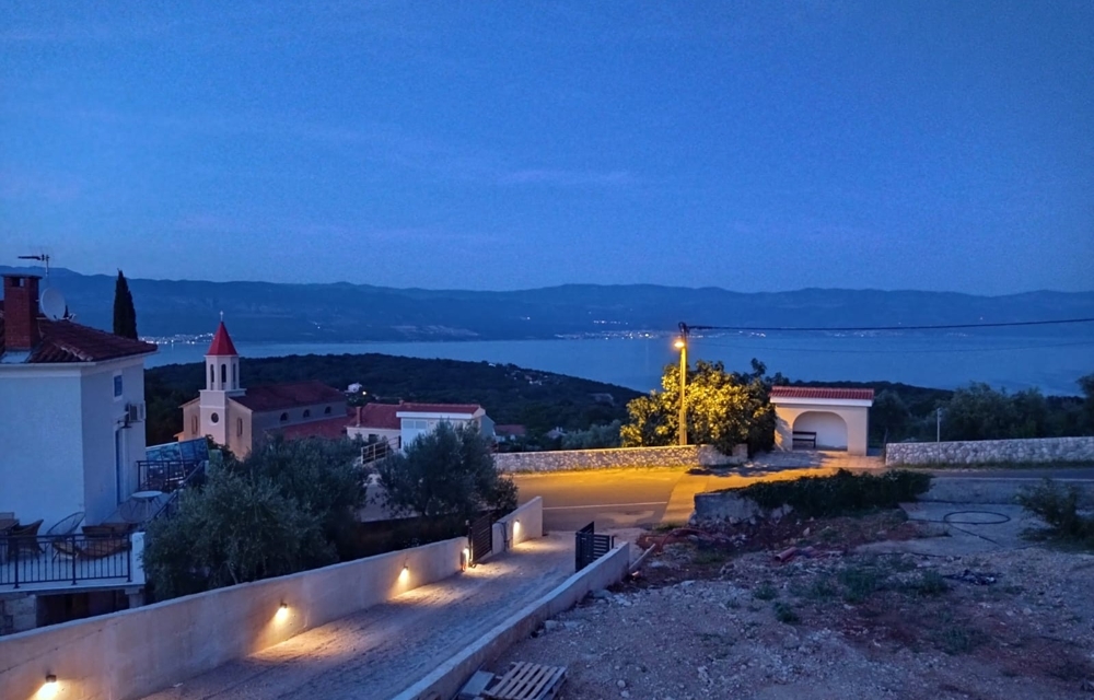 View from the property in Croatia of the sea at night, pool in the foreground and illuminated village in the background.