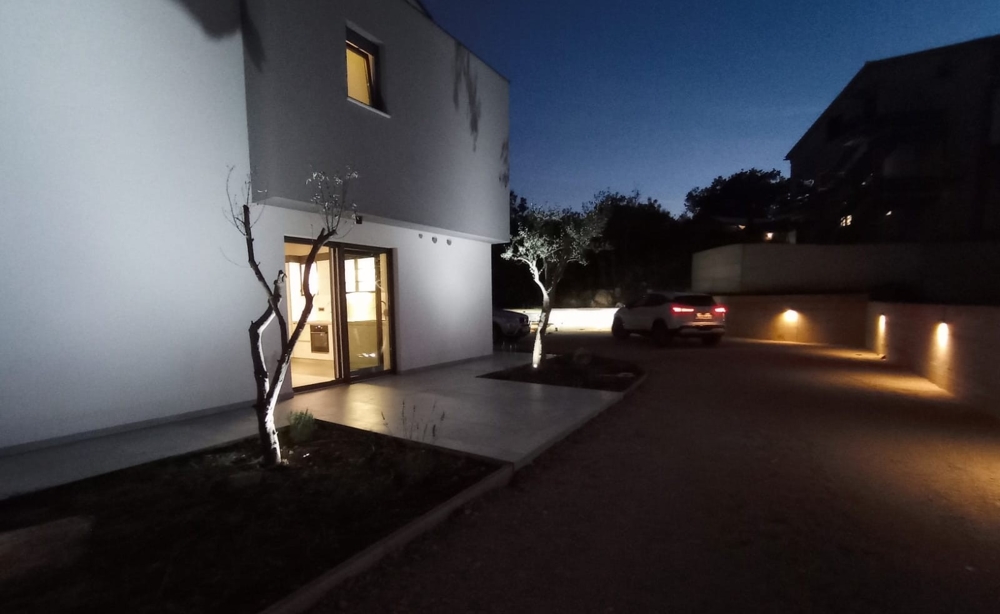 Night shot of a property in Croatia with exterior lighting and a parked car in the courtyard.