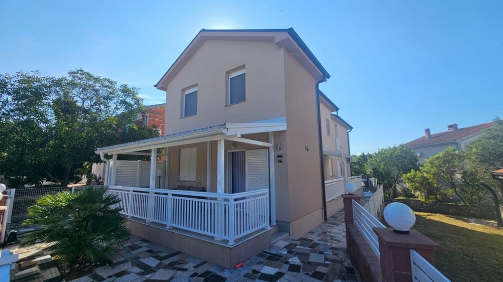 Detached house in Croatia for sale, side view with large veranda and surrounding garden.