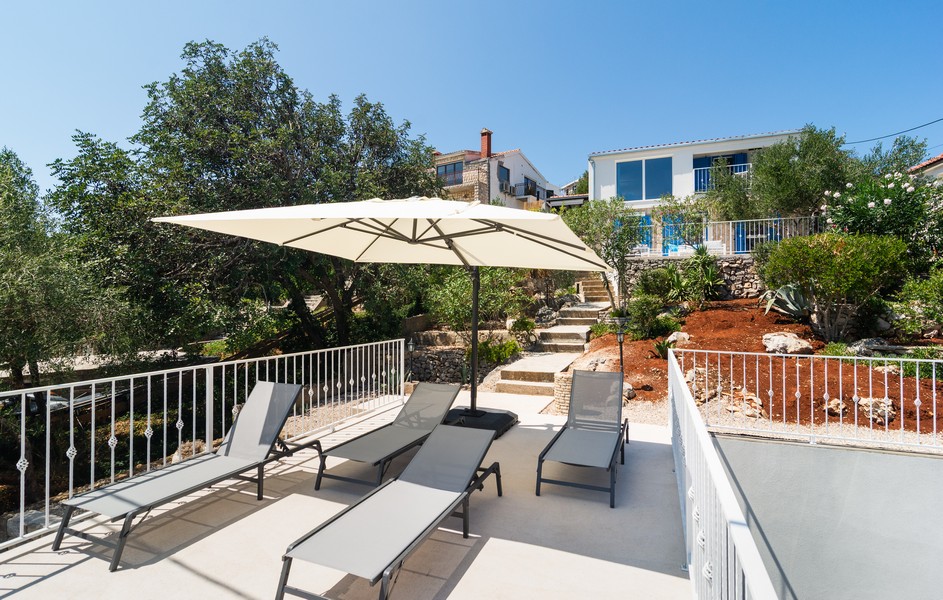 Terrace with sun loungers and parasol in front of the Mediterranean house