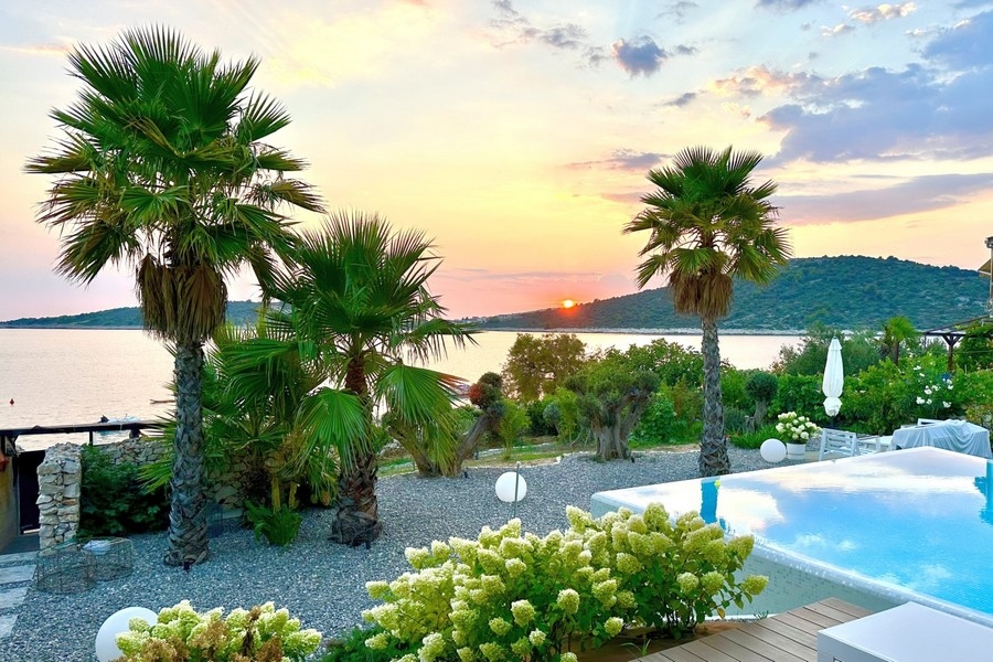 Sunset over the sea with palm trees and pool