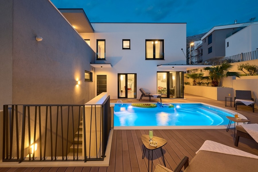 Pool area with wooden deck and illuminated villa