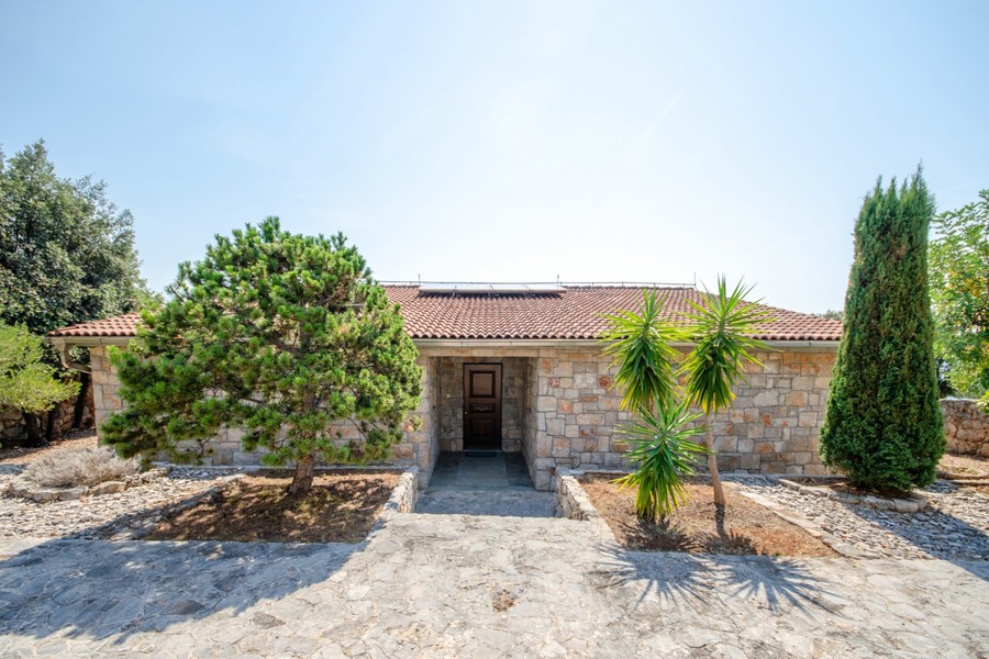 Entrance of the stone villa with palm trees and cypresses