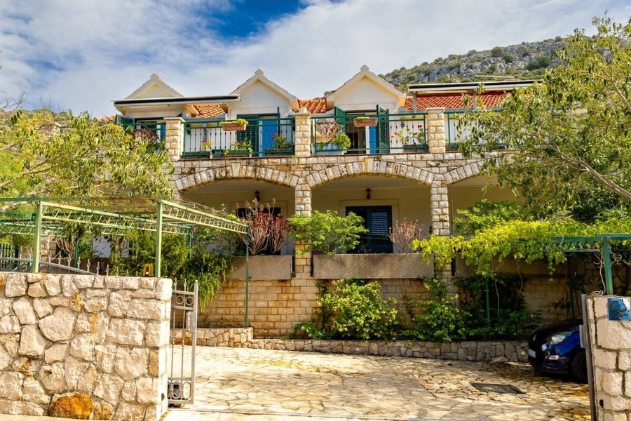 House with stone wall and driveway surrounded by greenery