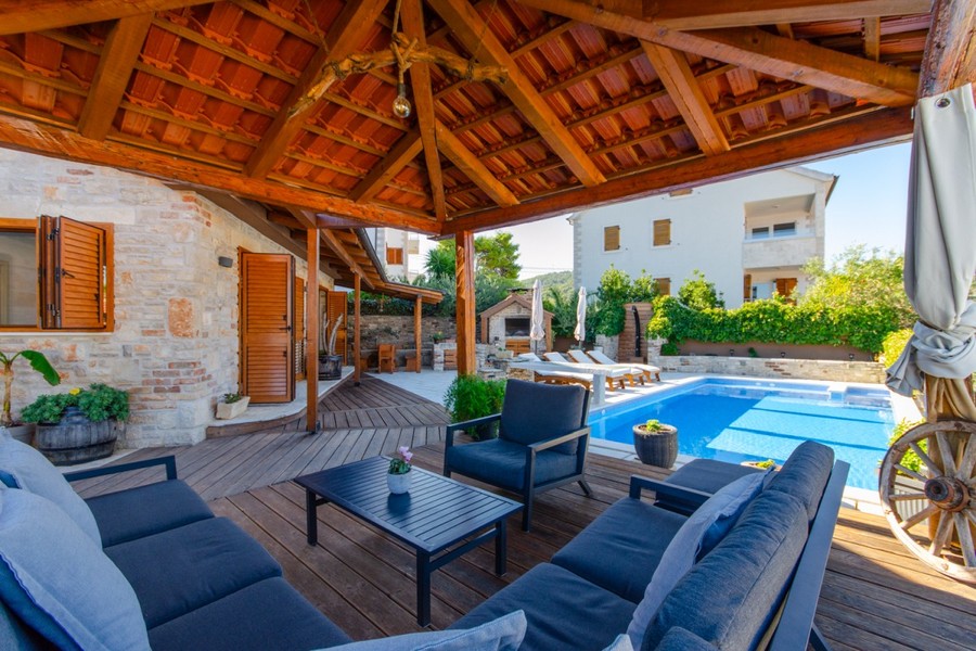 Covered wooden terrace with seating group by the pool